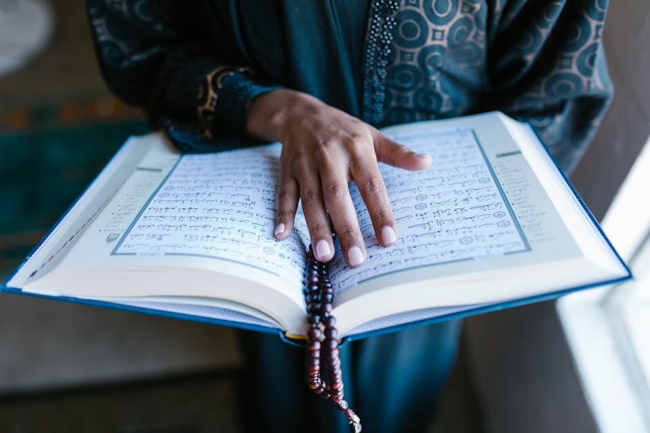 A woman's hand rests on an open Quran with prayer beads, symbolizing devotion.